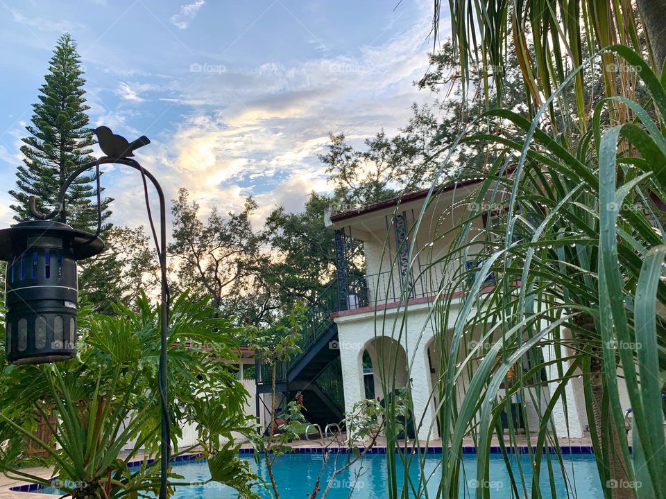 Gated white and red spanish old style architecture residential large house built in the early 1900s. Charming pretty style and beautiful landscaping with pool and chairs with great setting in a tropical environment with arched openings in patio area.