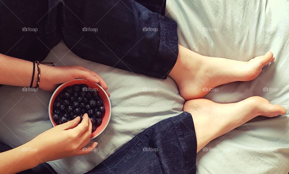 Woman with bowl of blueberries on bed.