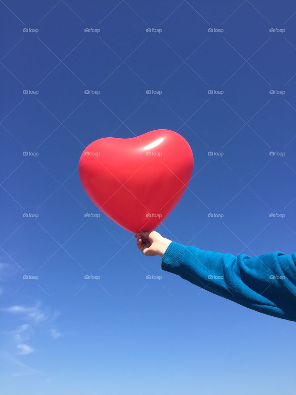 Person's hand holding heart shape balloon