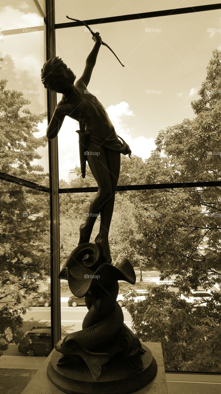 Silhouette of a statue shooting an arrow in to the city sky.