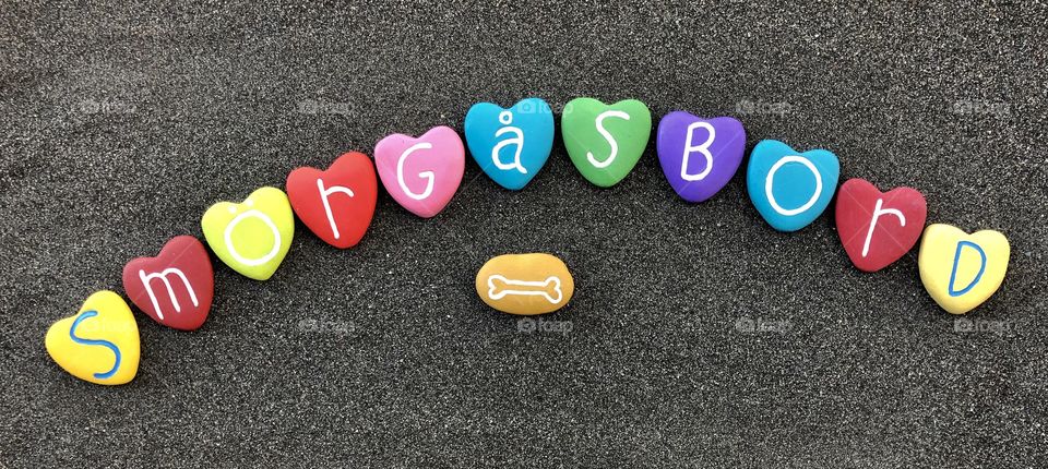 Smörgåsbord, swedish buffet text with multicolored heart stones over black sand
