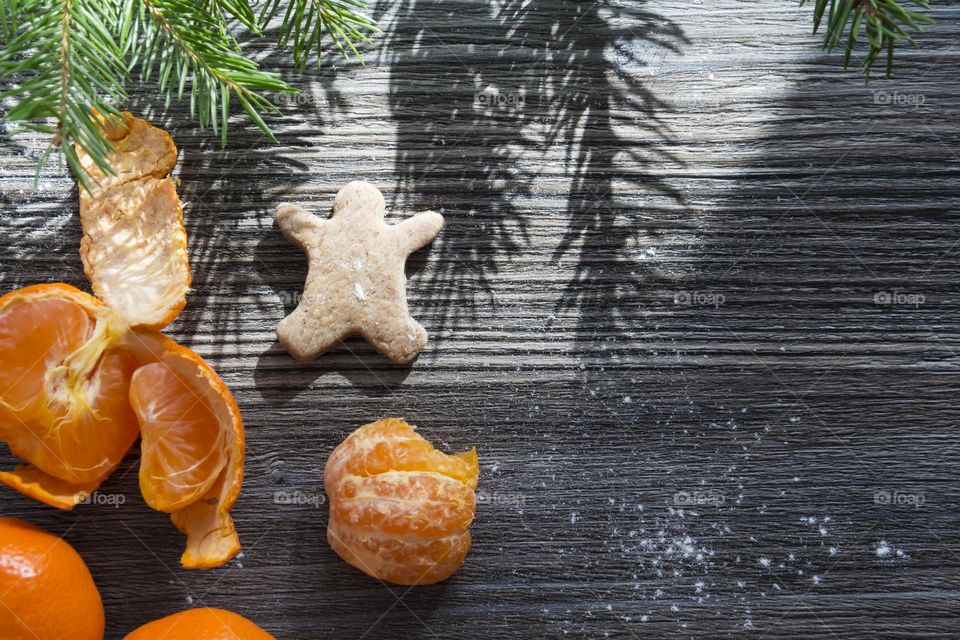 Christmas, gingerbread cookies on a wooden table sprinkled with flour, with tangerines and a green Christmas tree.