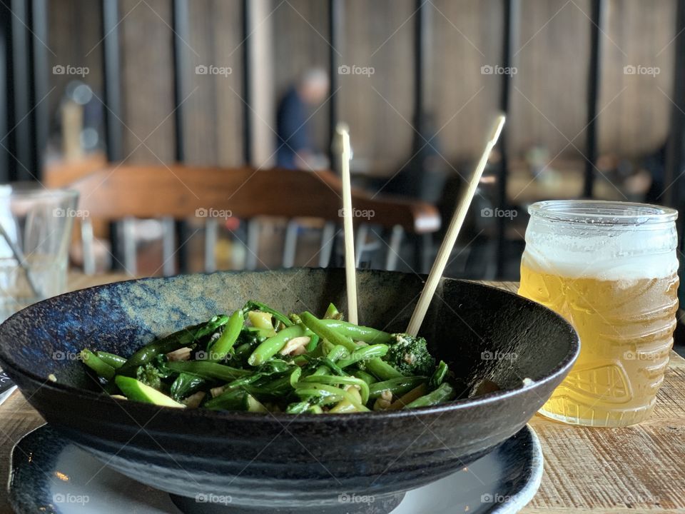 Asian healthy green food in a bowl with chopsticks served with draft beer 