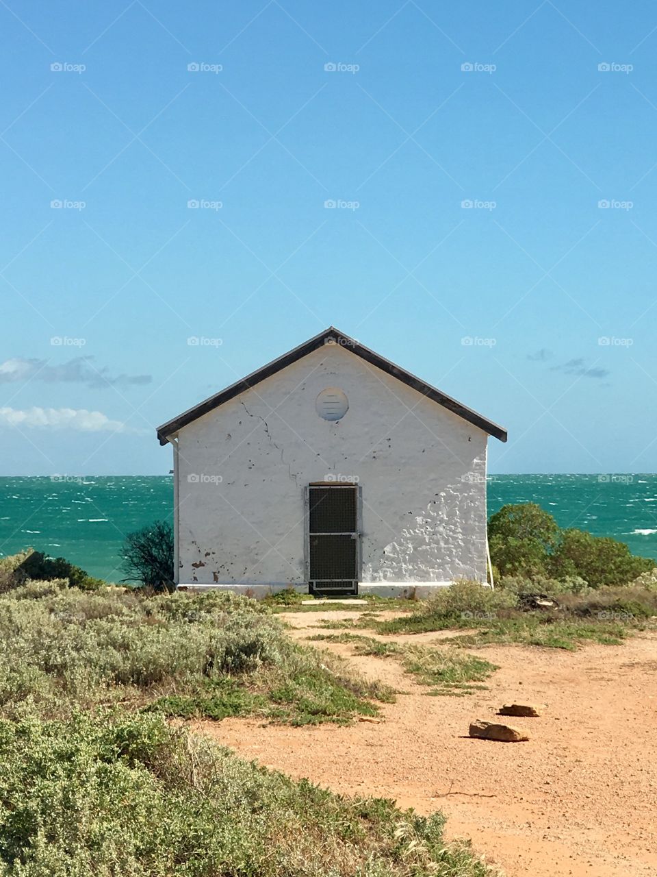 Old Lighthouse keepers house, white stone on vivid sky blue day with ocean horizon in background 