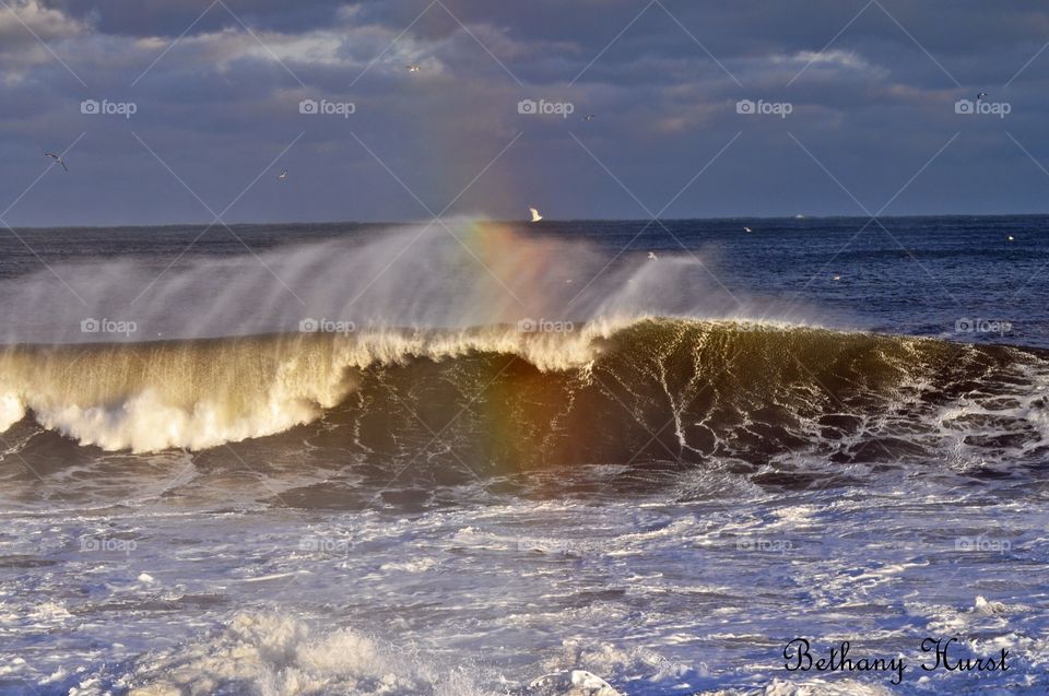 ocean delight. waves crash on the backshore as a rainbow reflects in the spray