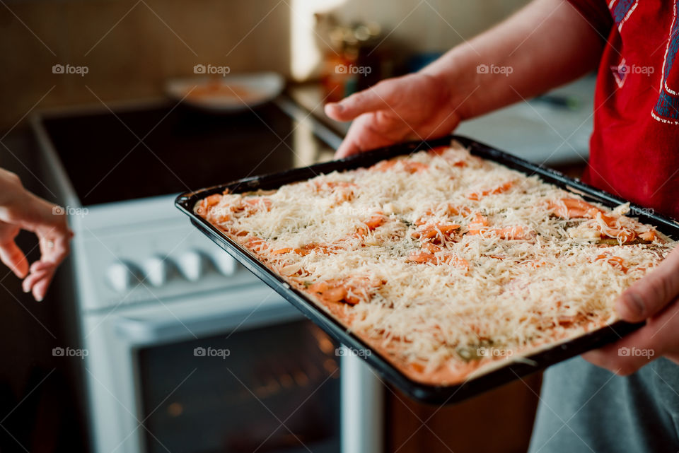 Cooking pizza with cheese at home. Men's hands hold a baking tray with pizza in front of the oven