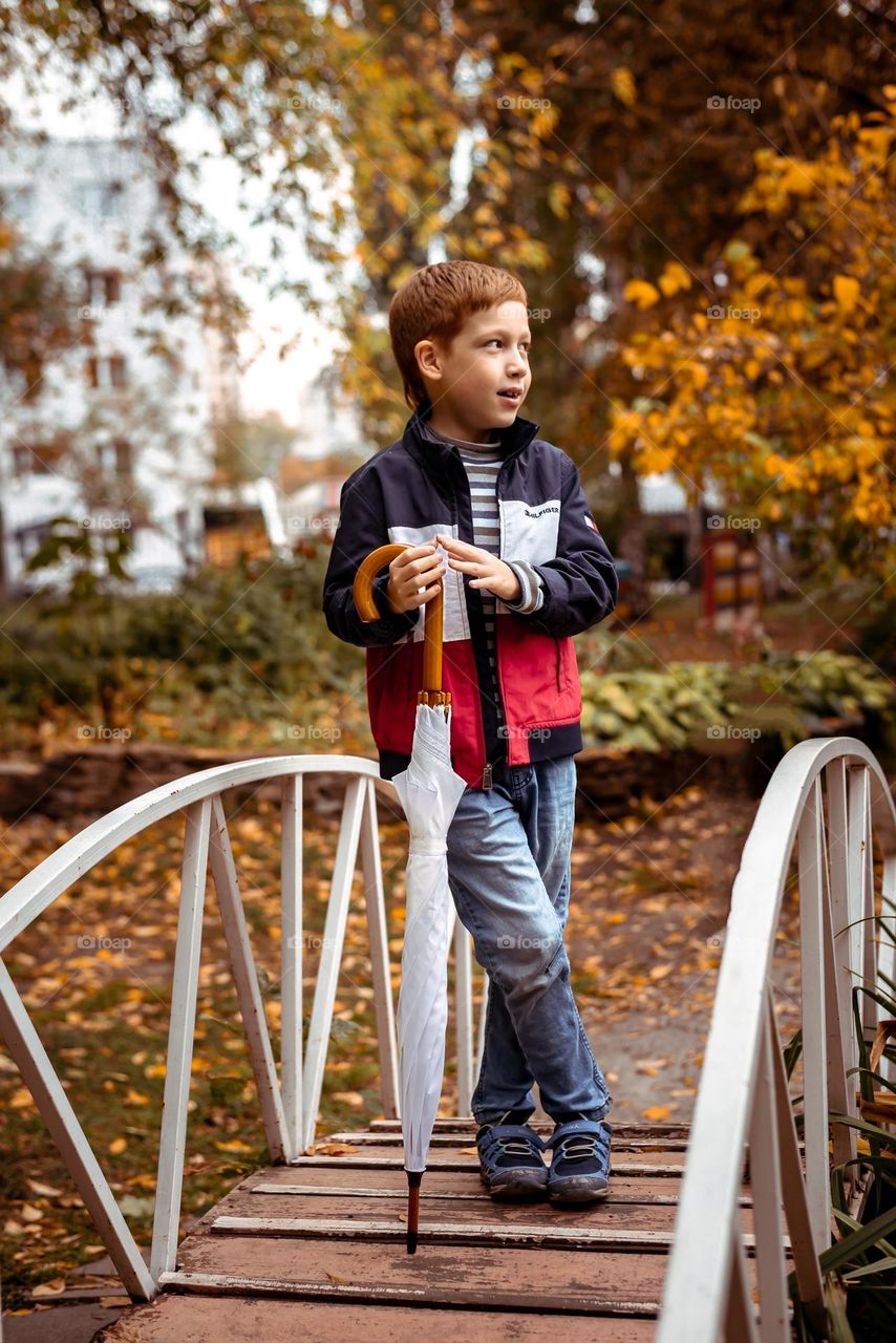Full length portrait child boy in autumn park on the bridge with umbrella