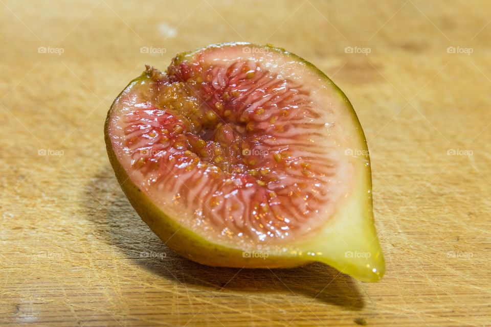 Horizontal photo of a close up on a half of a cut fig on a wooden cutting board
