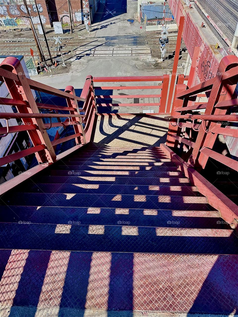 This is the view down the steps of the red metal staircase of the “Pulaski Bridge” at “Newtown Creek” in LIC, Queens. The shadows cast by its geometric structures create interwoven patterns that are quite beautiful. 2024. Hypnotic Productions