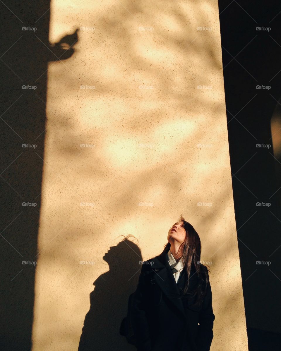 Woman standing against wall and looking up with shadow