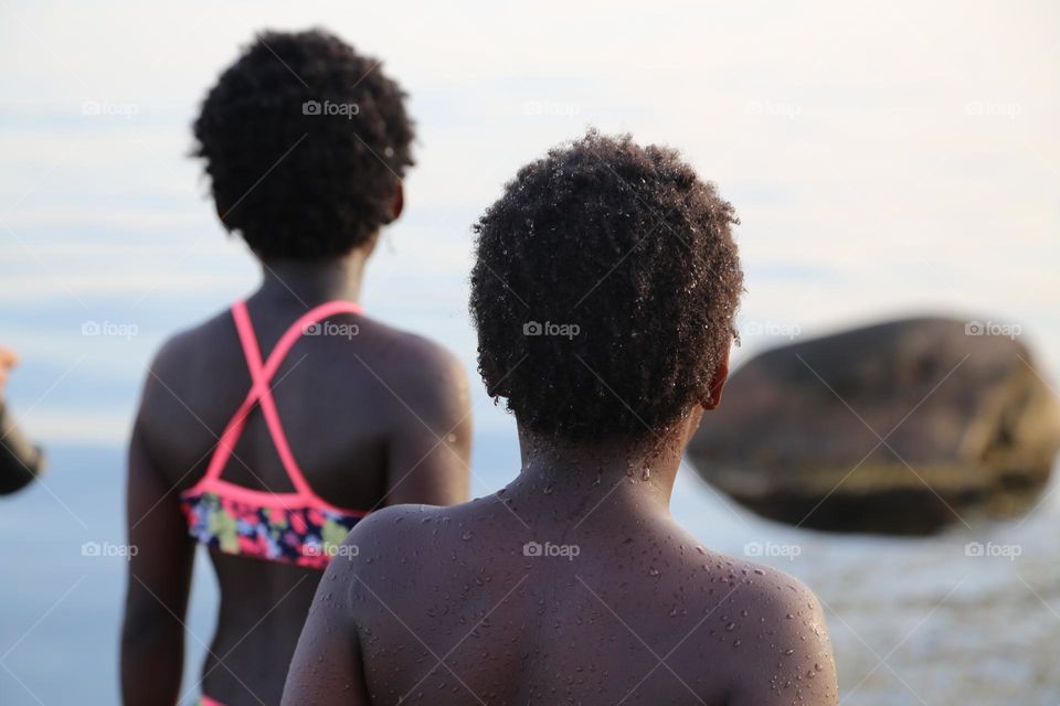 Siblings with brown curly hair at the beach looking at the sea 