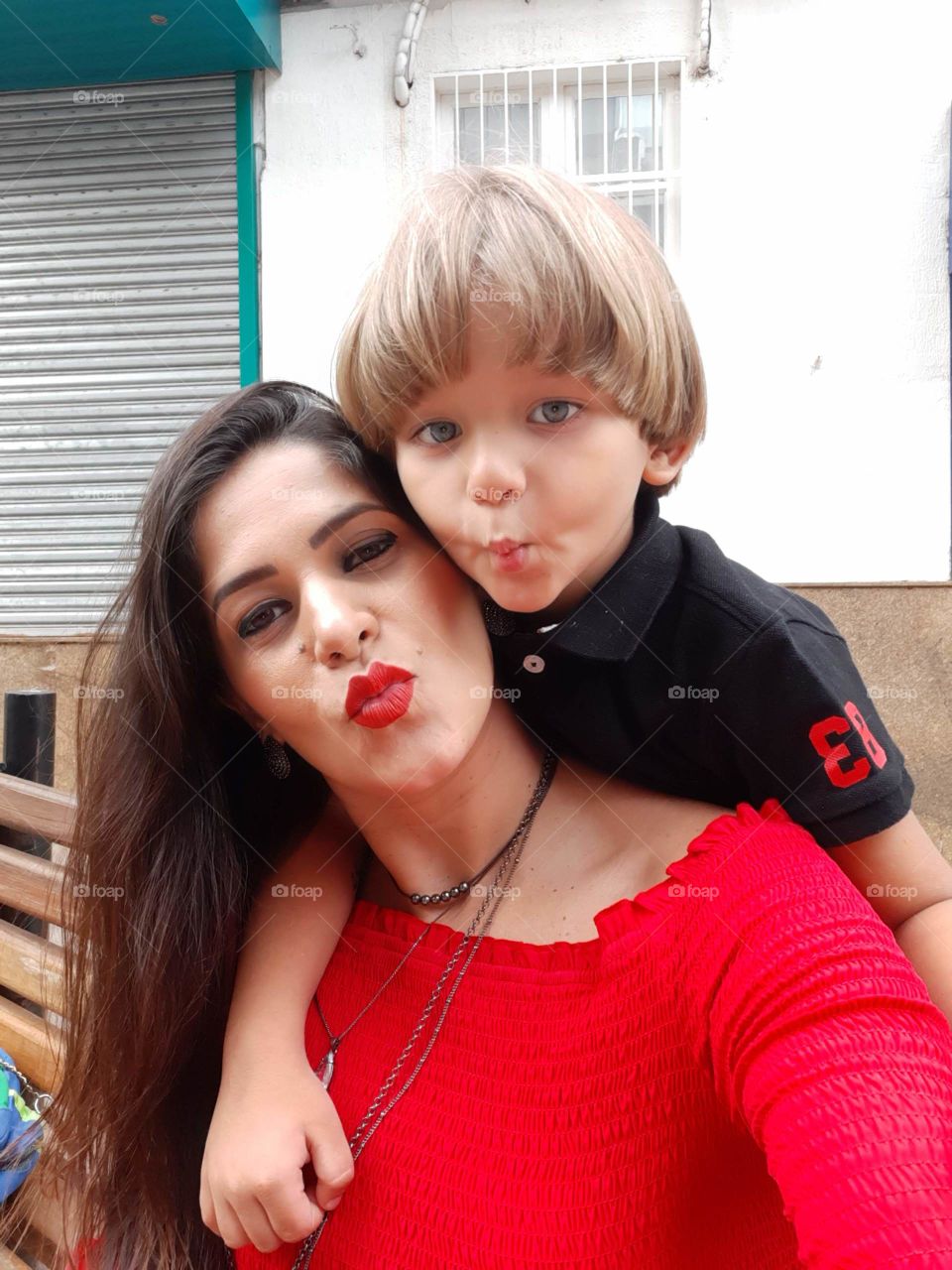 mother with red lipstick and blouse and son holding each other