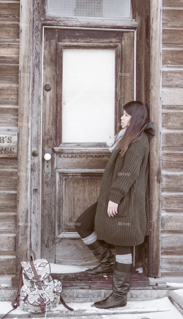 Lady waiting patiently in front of an old wooden door feeling cold