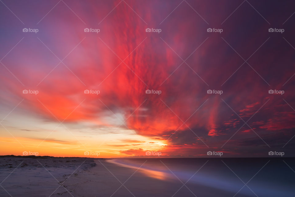 An incredibly vibrant colorful sky just before the sun rises over a beach. Pink and orange colors reflecting in the silky smooth water
