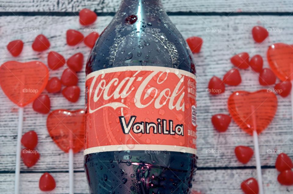 A plastic bottle of Coca-Cola vanilla with candy hearts and a white rustic