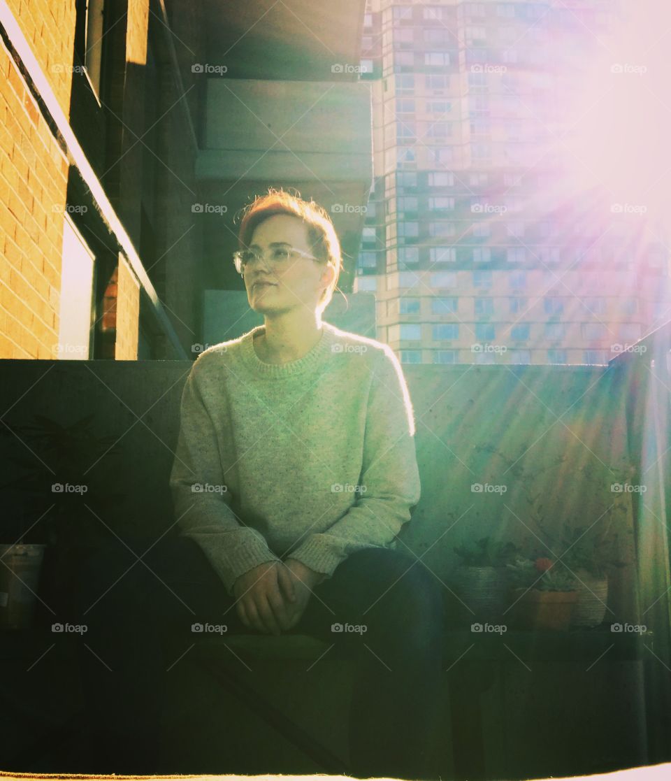 Short red hair young woman sitting on balcony with sun burst Wearing a sweater and glasses