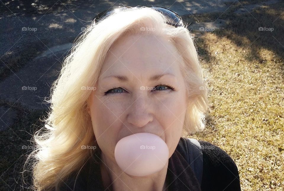 Woman outside in the sunshine blowing a bubble wearing eyeshadow & makeup