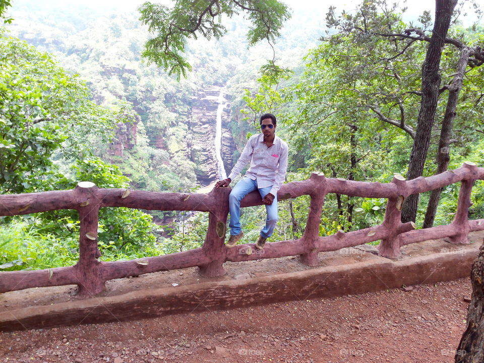Man sitting on wooden fence in front of waterfall