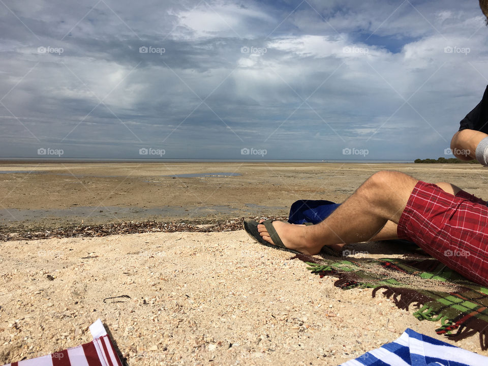 Man laying down on remote south Australia beach, legs and shorts showing 