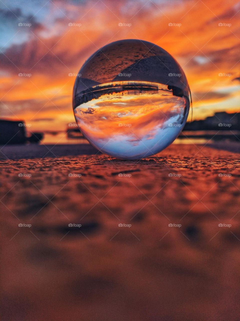 Top view of lensball, crystal ball on the beach,  seashore close up. Reflection of beautiful red sunset sky in lens ball.  Abstract