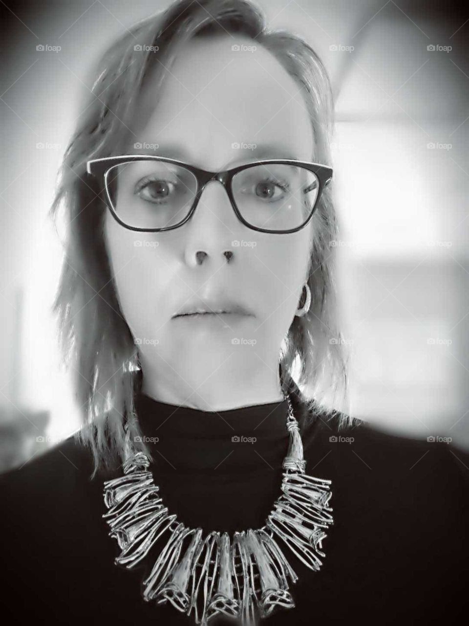 a serious woman wearing eyeglasses and a necklace