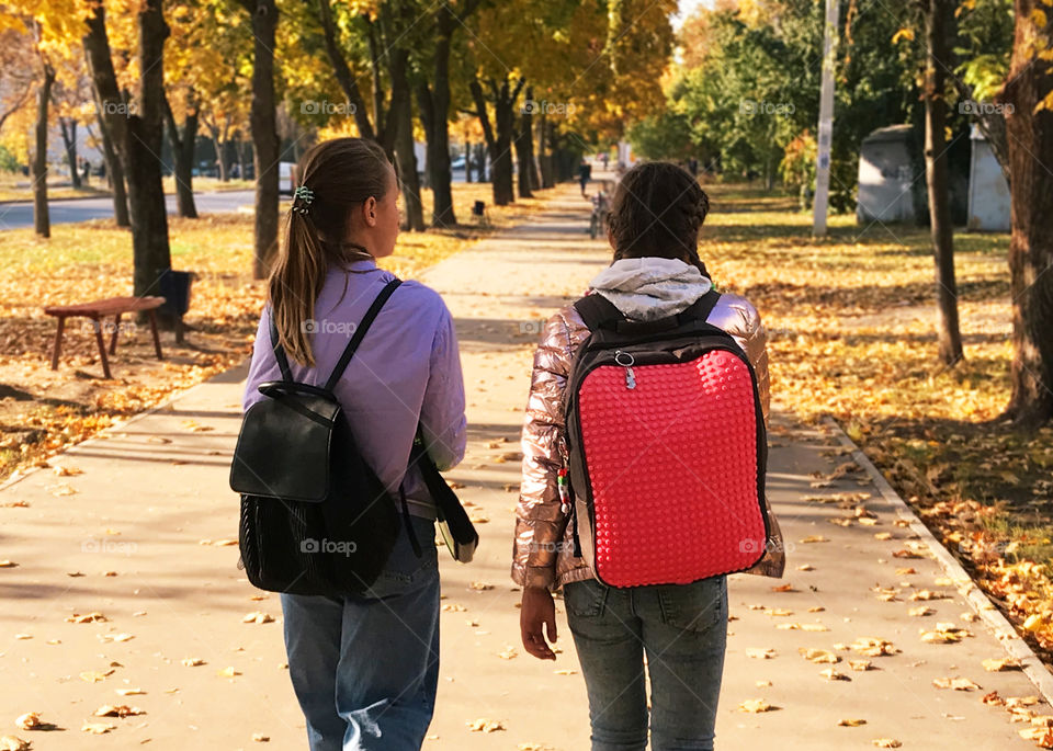 Young students with backpacks walking together by the autumn street 