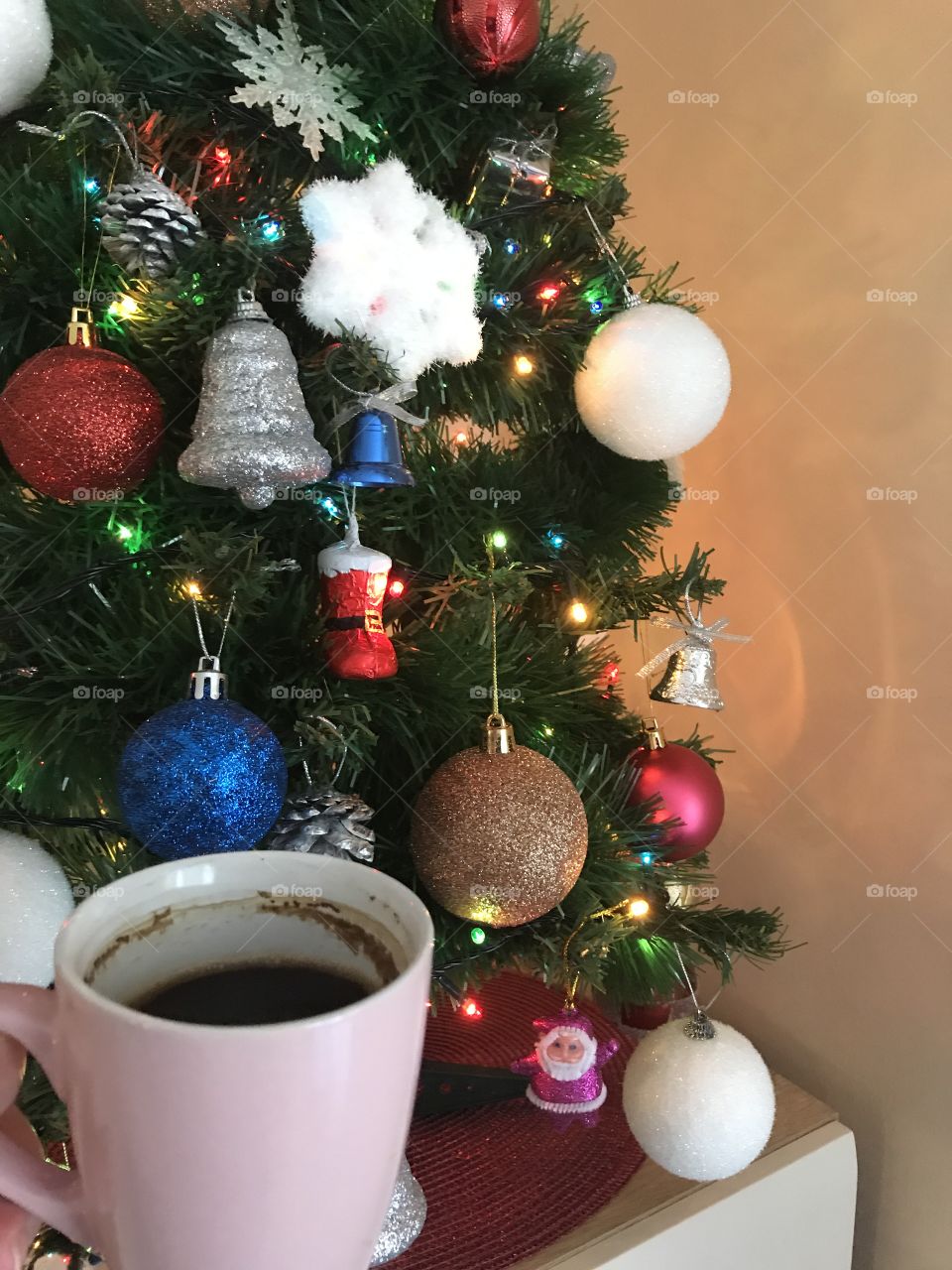 Christmas tree and the light pink cup of coffee beside the Christmas tree. Christmas coffee and colorful and shiny christmas tree.