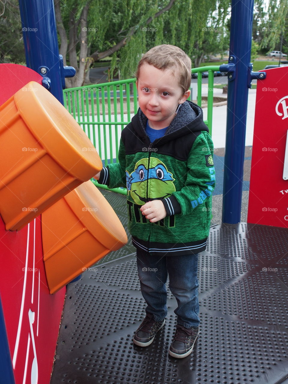 A little boy enthusiastically plays on the plastic drums on a play structure in the park. 