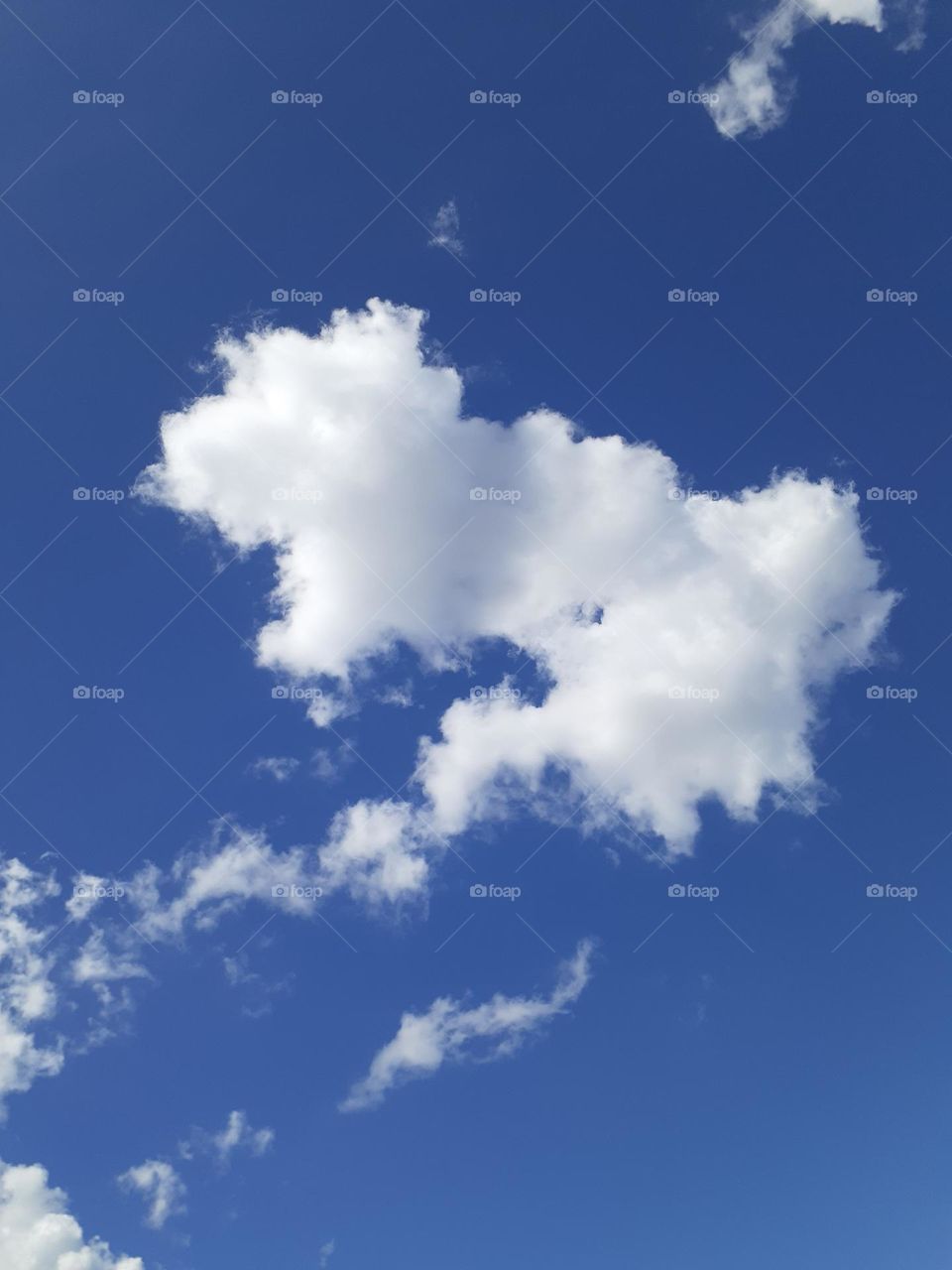 White clouds in a dark blue sky. The main cloud in the picture looks like a rooster eating a trail of food.