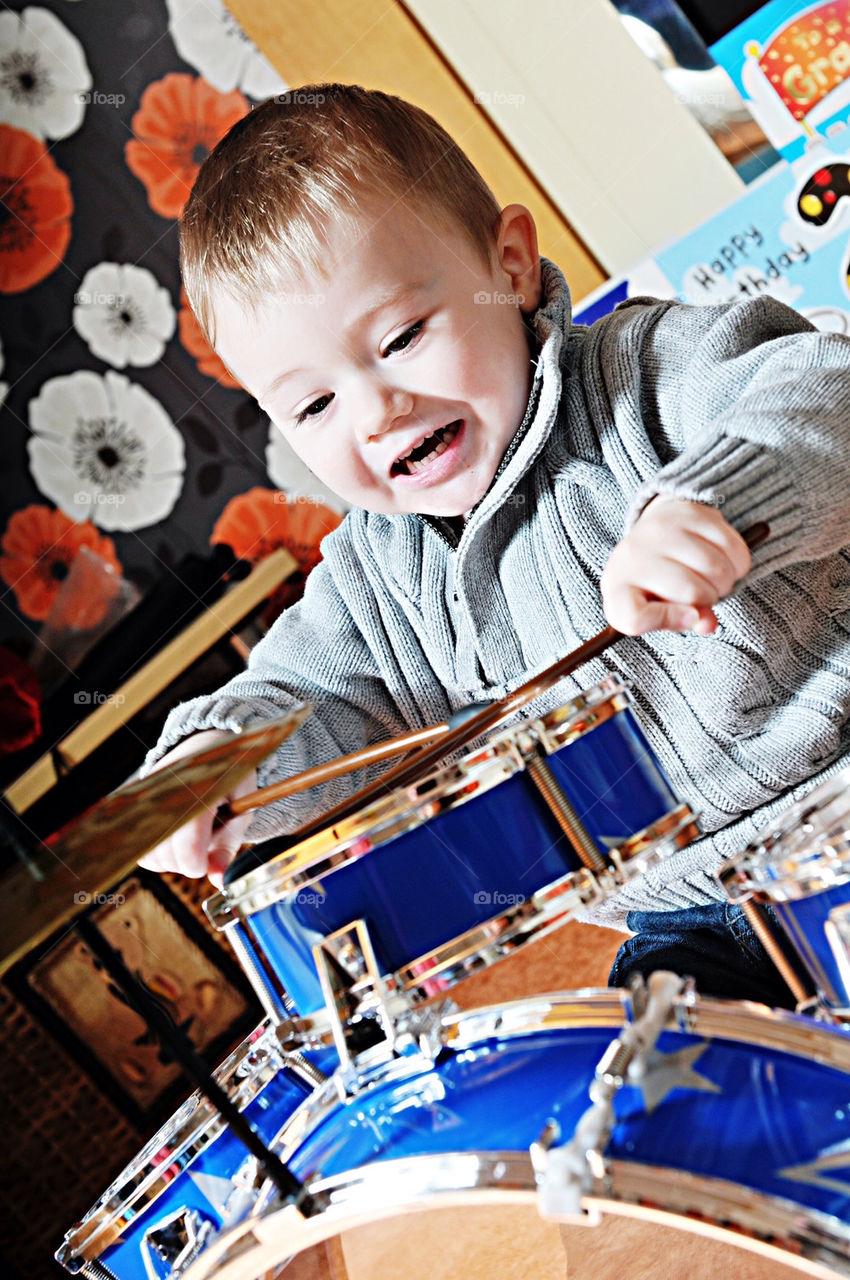 A YOUNG WHITE BOY, AGED THREE, PLAYS A DRUM KIT LIKE A ROCK STAR.