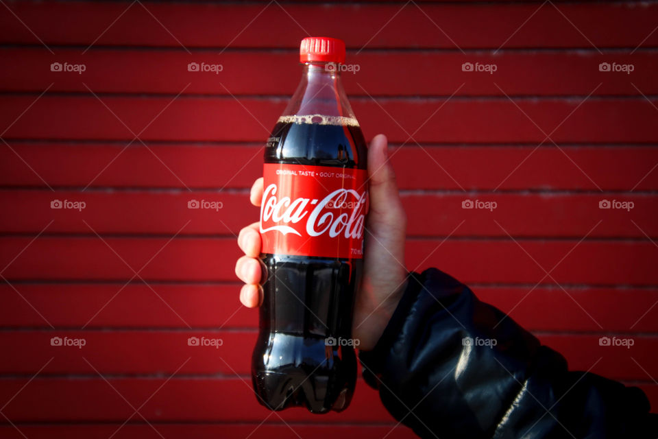 Man's hand holding a bottle of a Coca-Cola