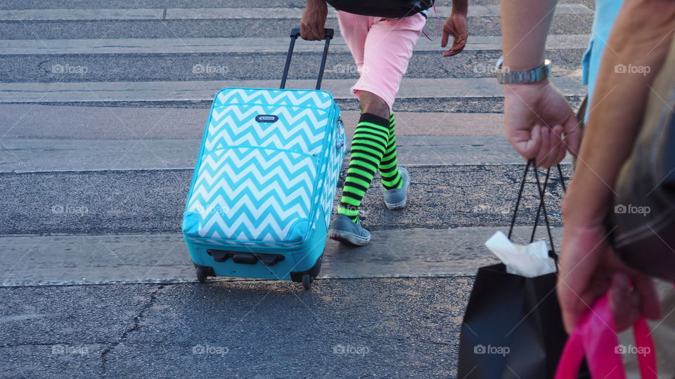 Crazy colorful tourist luggage. Street scene of a man in weird clothing dragging luggage bag 