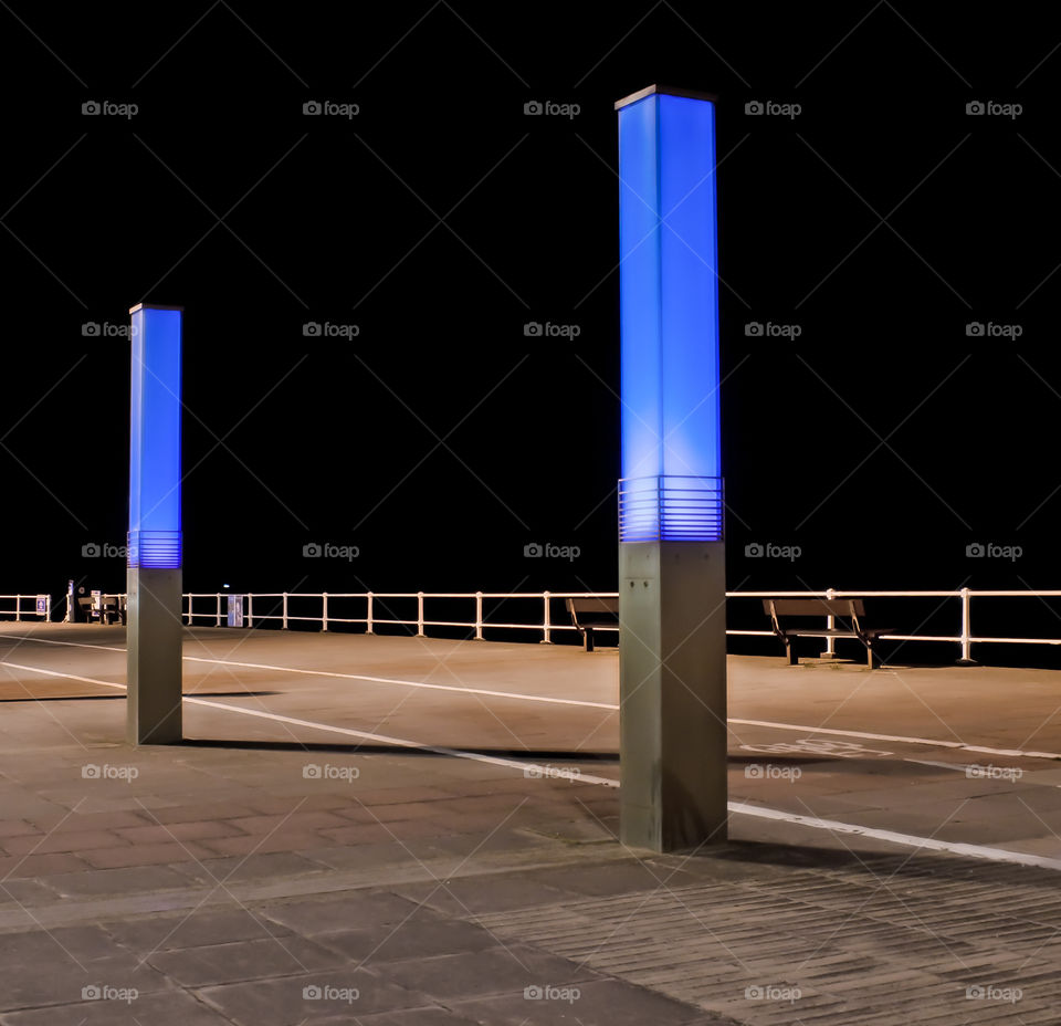 2 lit up pillars, form part of an artistic street lighting display, glowing blue against the dark night sky