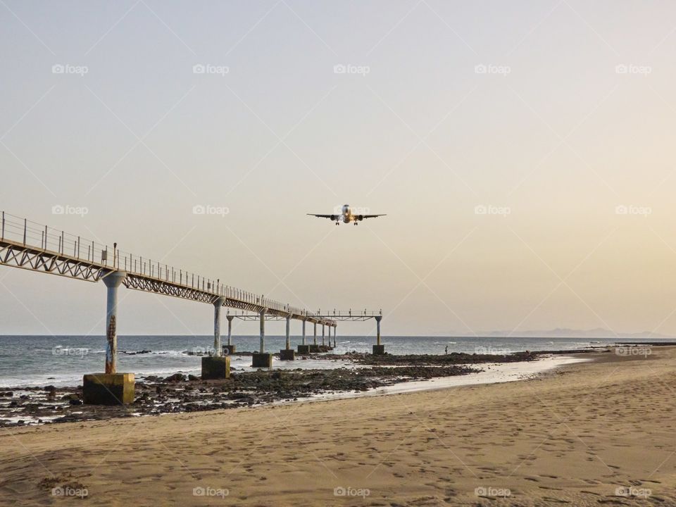 Paisaje se playa con avión aterrizando con una luz del atardecer muy agradable, y piedras en el entorno