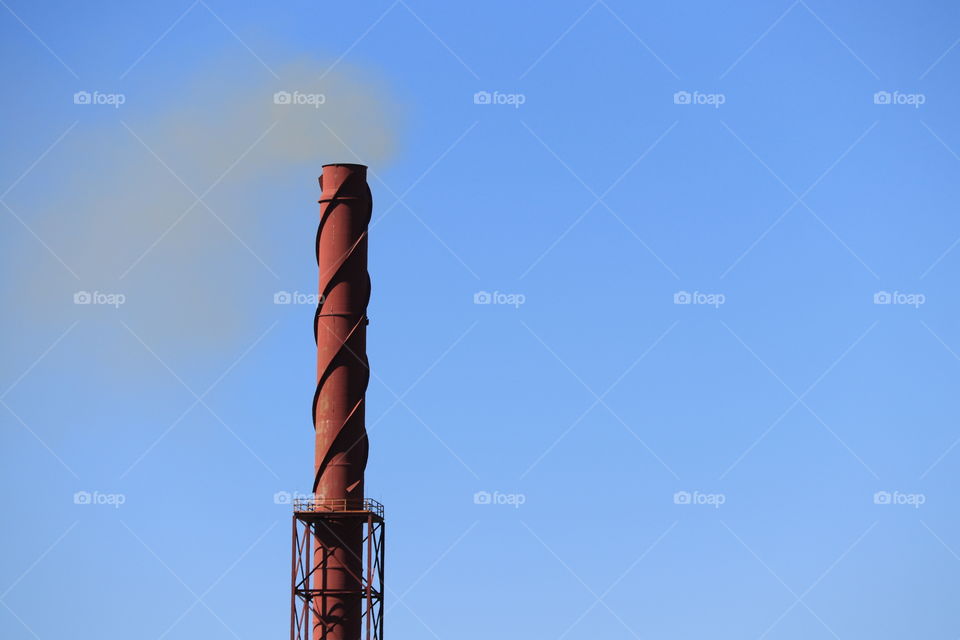 High rusted iron ore industry chimneystack tower blowing smoke into clear vivid blue sky 