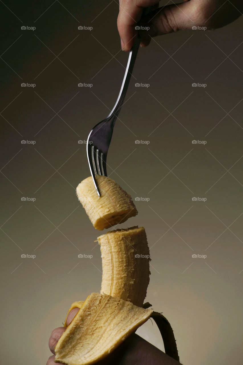hand sticking a fork to a banana