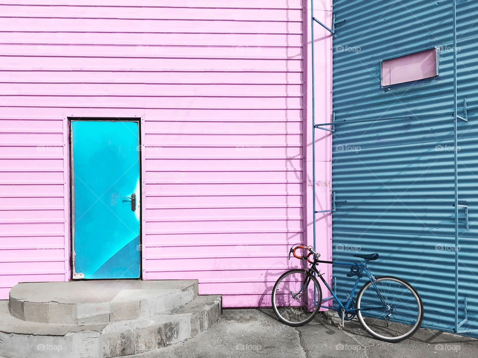 Bicycle standing in front of a striped pink and blue building 