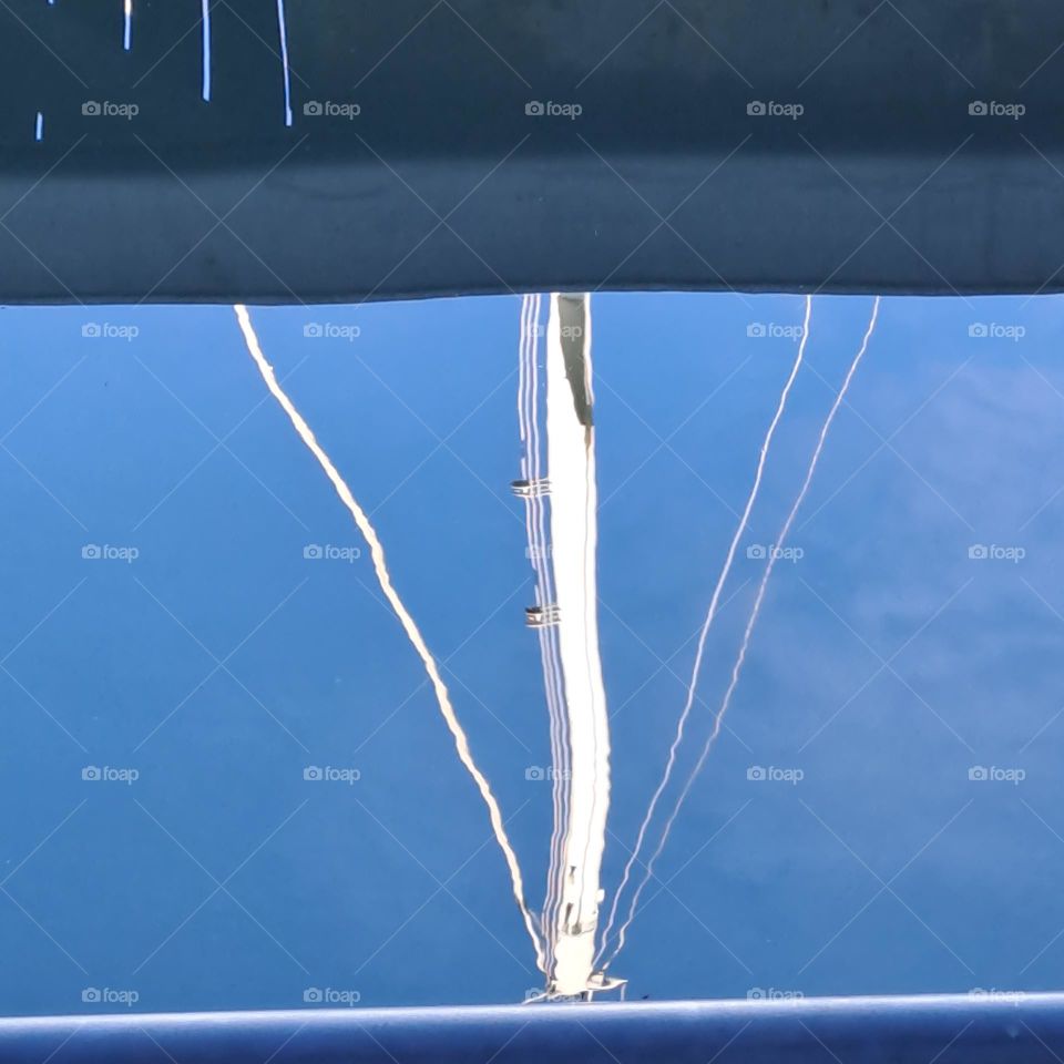 boat mast and blue sky of bright October day reflected in still calm.sea water. uk coast.