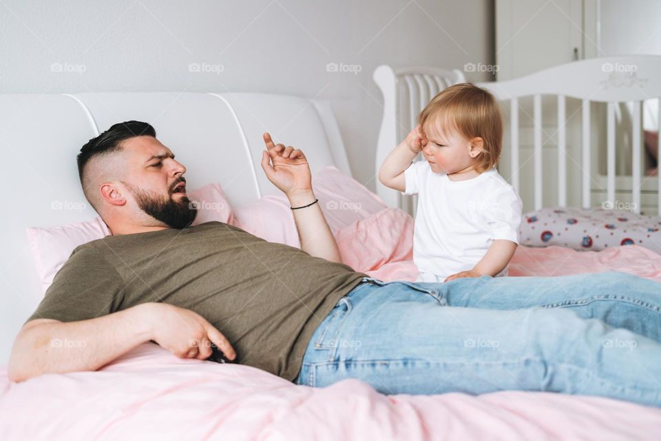 Strict father young man and baby girl little daughter on bed in room at home