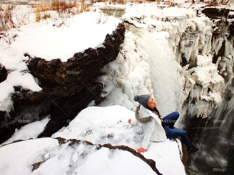 Girl sitting by the frozen icy Waterfall