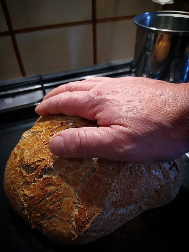 Homebaked bread.  A man's hand lies on the baked bread