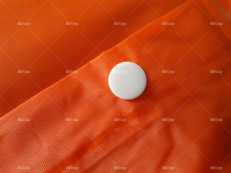 Close-up of button on orange raincoat