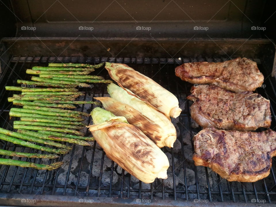 Grilling steaks, corn, and asparagus over charcoal.