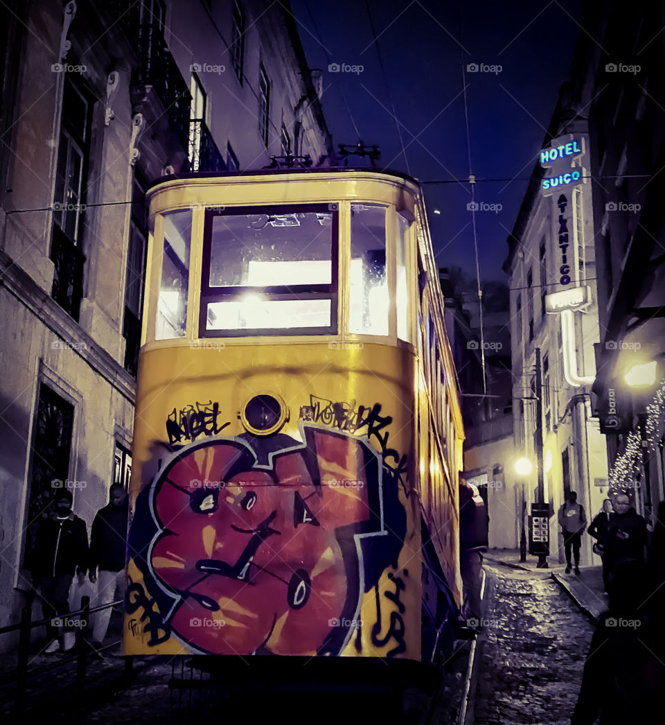 A nighttime, winter view of the Glória Funicular ascending towards Hotel Suiço-Atlantico, the car is bright yellow again the dark sky