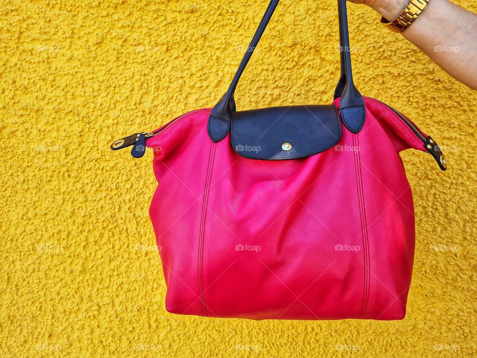 hand holds hot pink glitter bag on yellow background