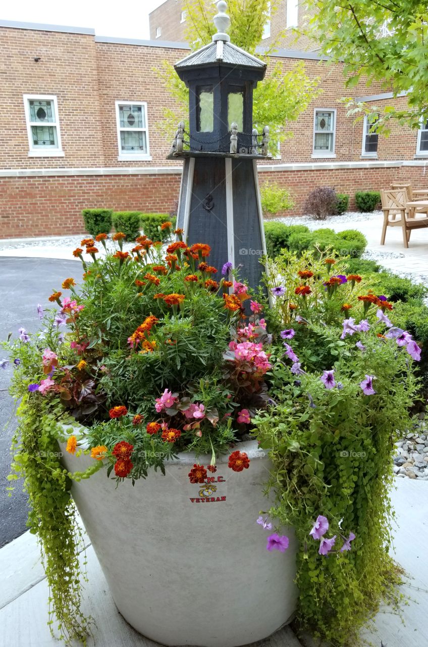 Flower arrangement. Large outdoor flower pot with lighthouse in center.