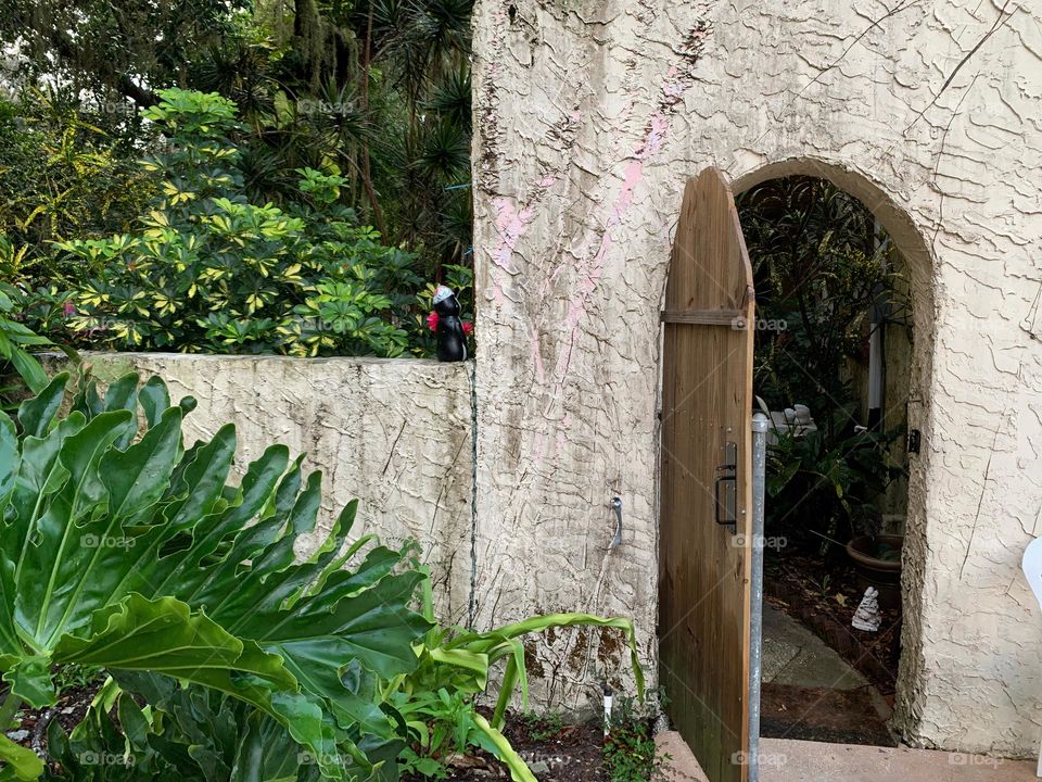 White and red spanish old style architecture residential large house built in the early 1900s. Doorway with antique style wood door in a stairway wall seen from tropical plants and live oak trees leading to another garden.