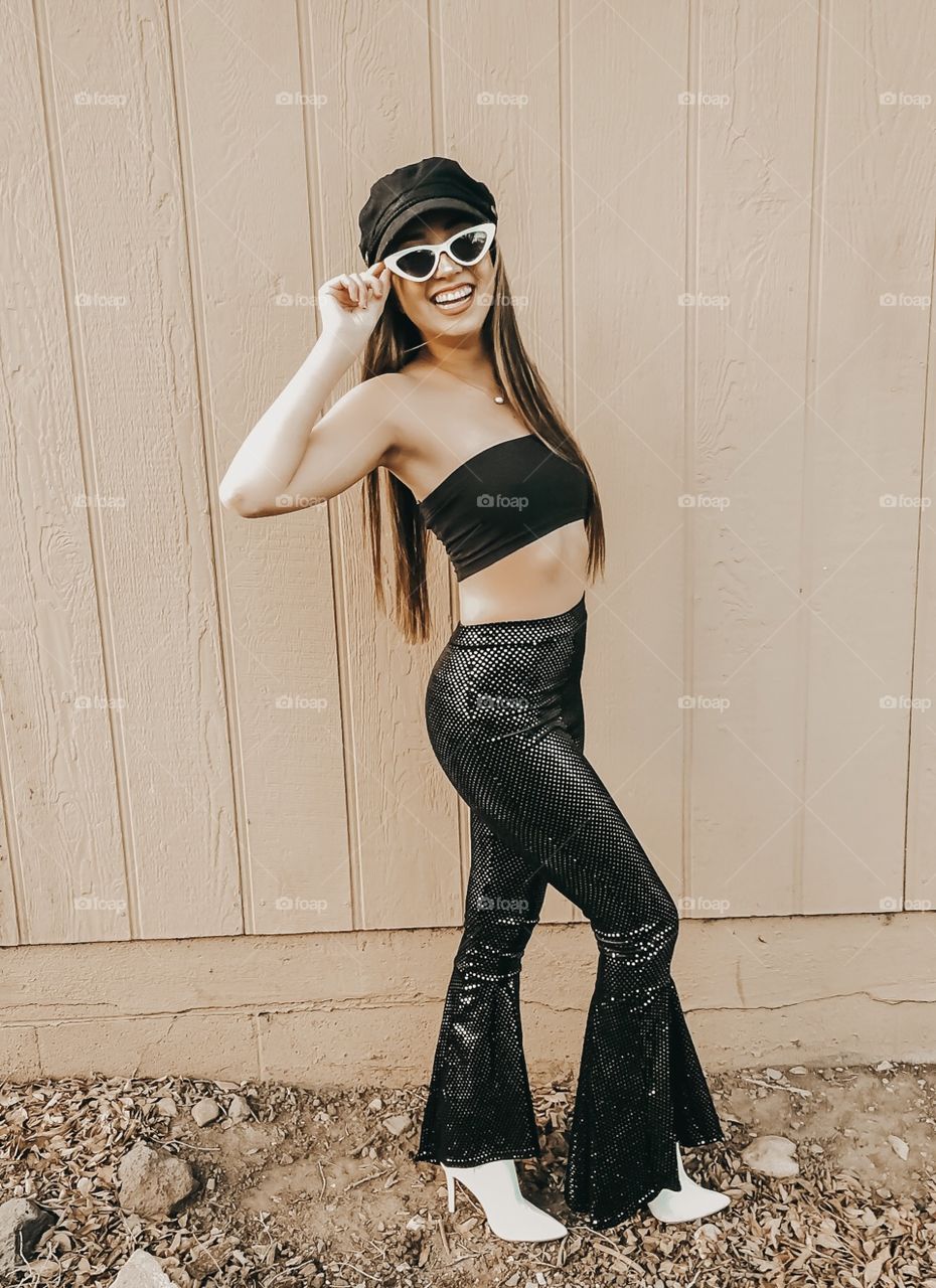 Young girl dressed up in retro clothing with sequin bell bottoms and funky white sunglasses.
