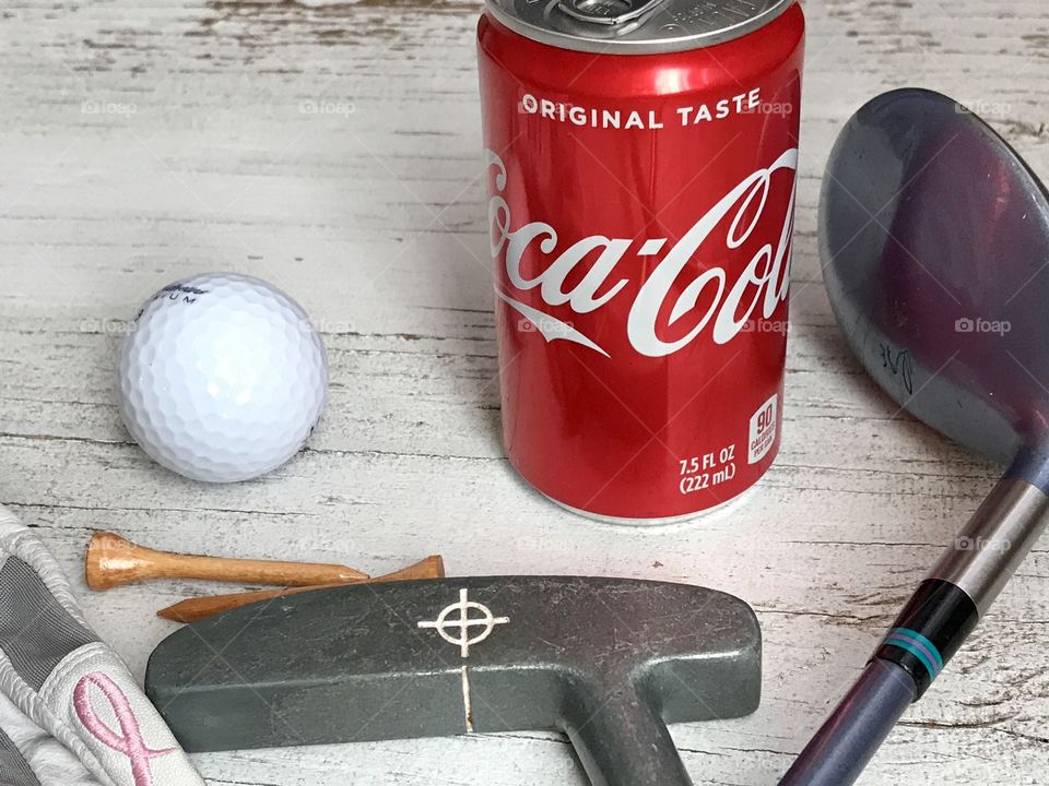A can of Coca Cola with golf equipment on a rustic white background 