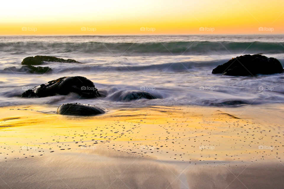 Long exposure sunset image over boulder beach with sun reflecting on the sea sand. Image from Cape Town South Africa